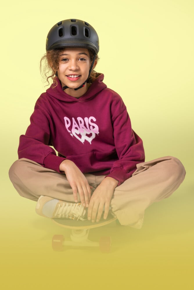 Meisje met zwarte READY-kinderhelm van woom op het hoofd zit met gekruiste benen op een skateboard.
